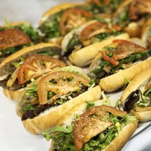 Mini sub à la saucisse garni de provolone, oignons caramélisés, aubergines marinées, laitue et tomate